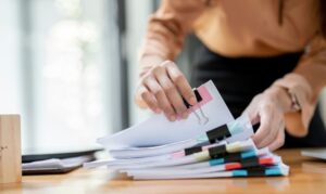 Woman hands working in Stacks of paper files for searching and checking unfinished document