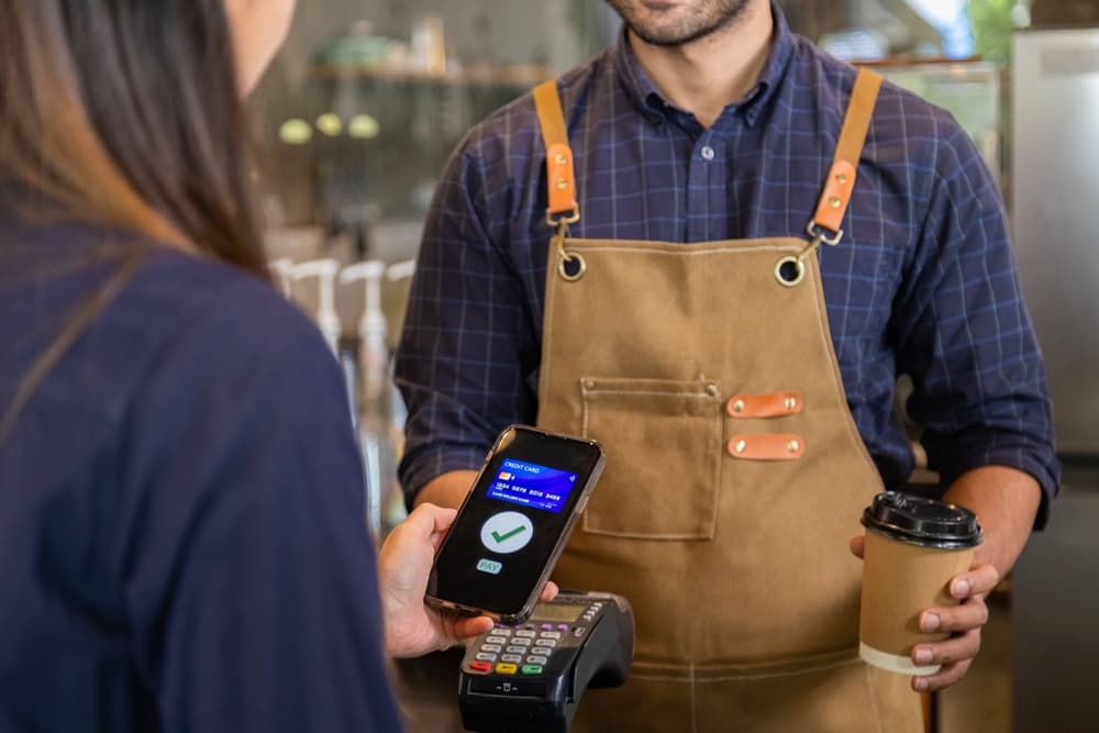 Man owner coffee shop submit an electronic cash register and coffee cup to woman customer